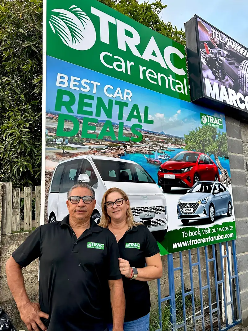 Two members of the TRAC team in front of a TRAC Car Rental sign